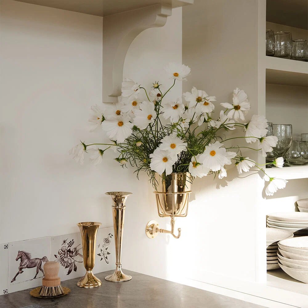 Opal Wall Vessel filled with white cosmos above brass bud vases on a kitchen counter