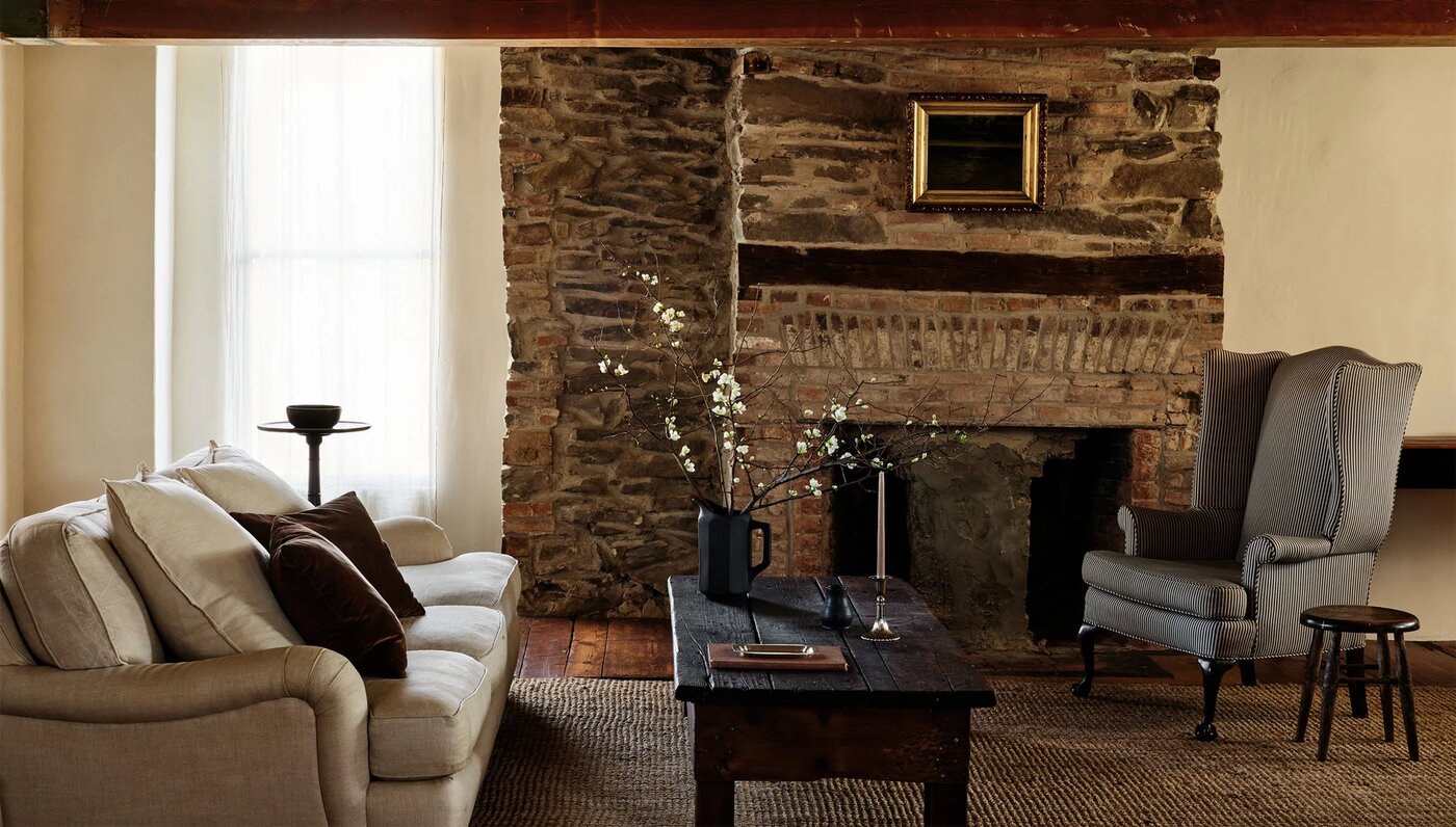 Stone fireplace in a living room with a wooden coffee table and a vase of branches