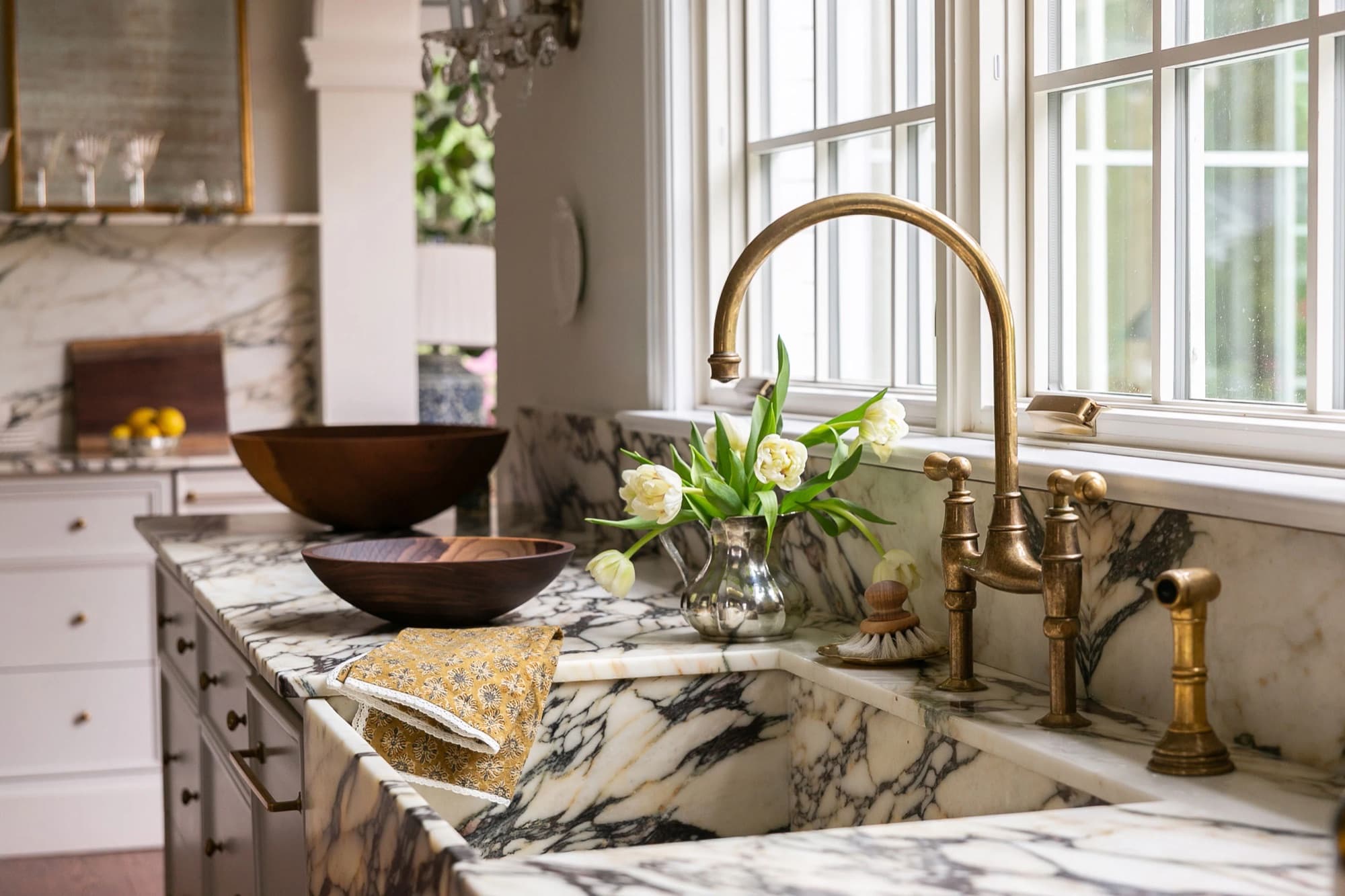 Antique brass bridge faucet over a marble sink with white tulips in a silver jug